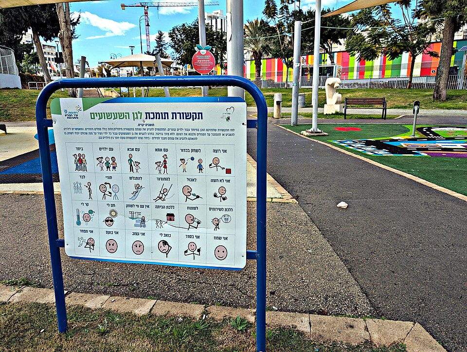 Un panneau de communication installé dans un parc public, portant des rangées de pictogrammes légendés sur un cadre métallique.